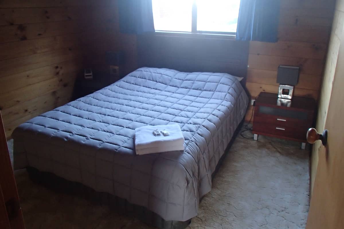 Un dormitorio con cama, mesita de noche y ventana con cortinas.