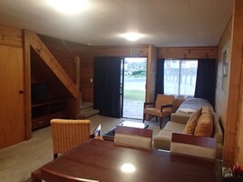 Interior em madeira com escada, um conjunto de sofá, uma mesa e um sinal de saída.