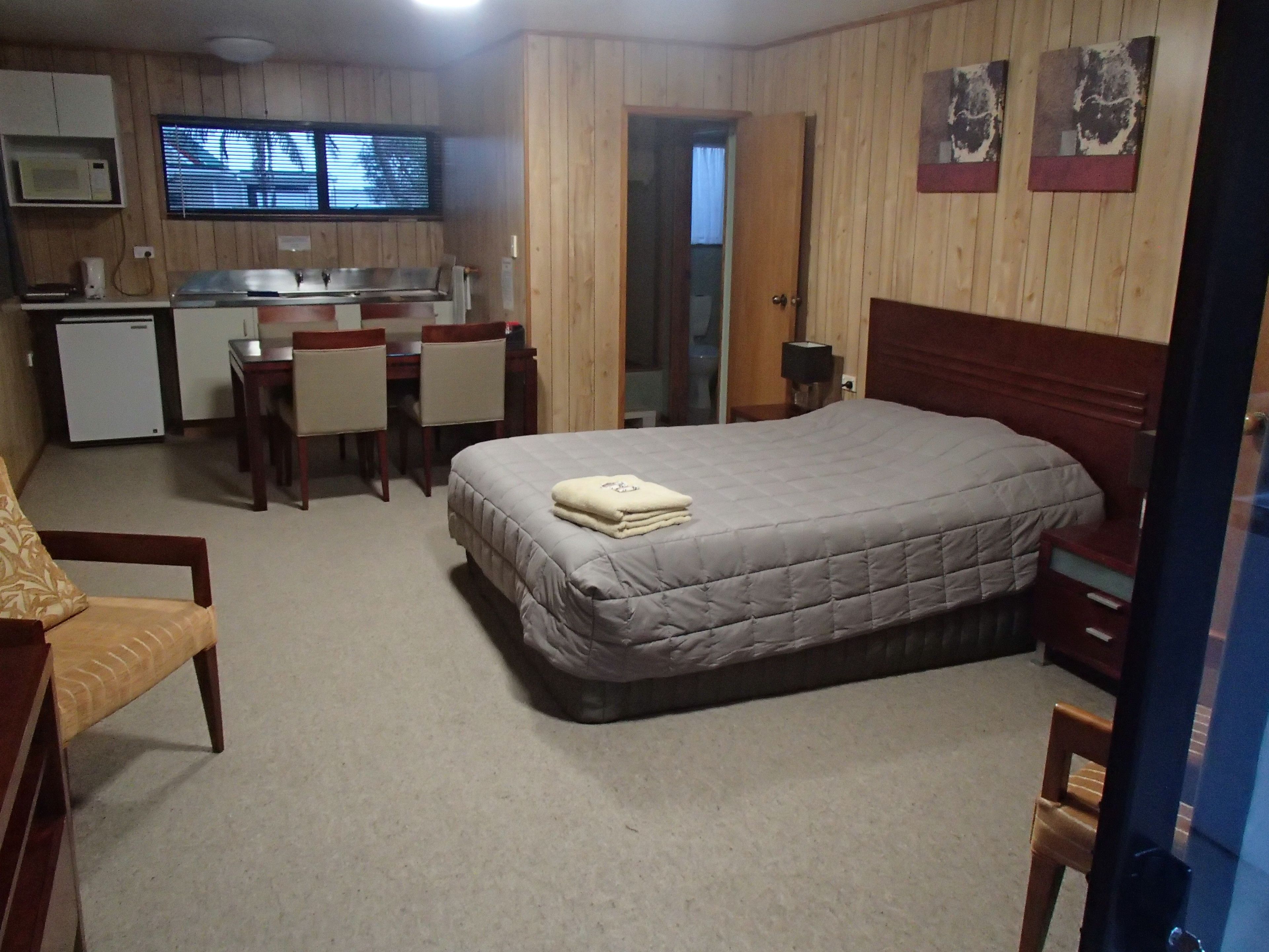 A compact hotel room with a single bed, a small kitchenette, a dining area, and a bathroom.