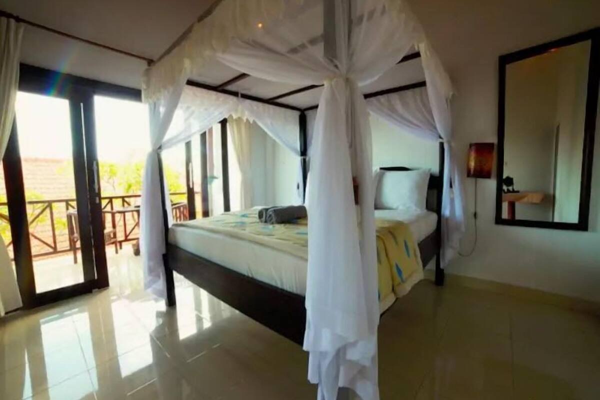 A bedroom with a four-poster canopy bed, a large mirror, and a balcony with a view.