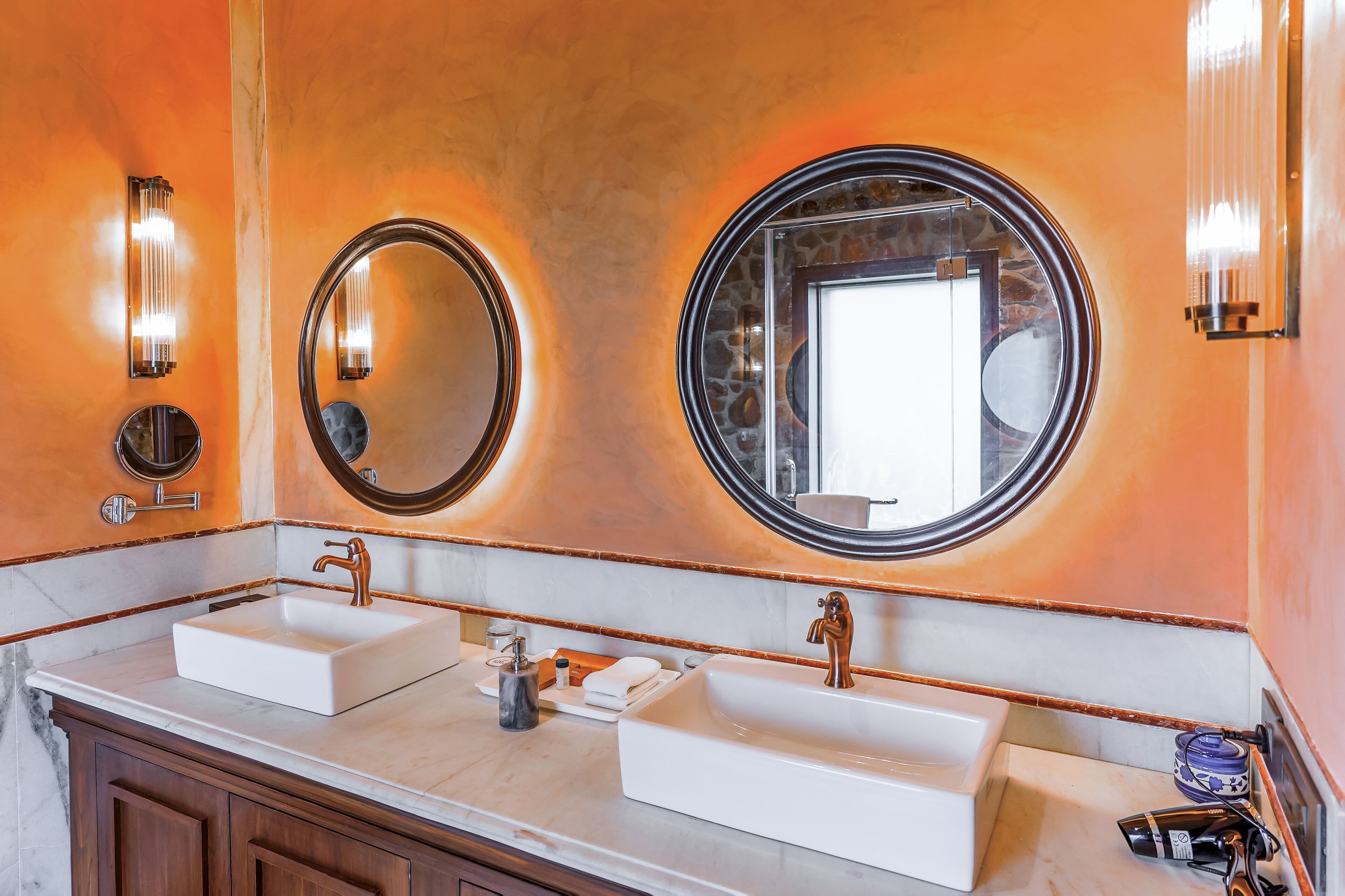 A bathroom with two sinks, a mirror, and wall sconces.