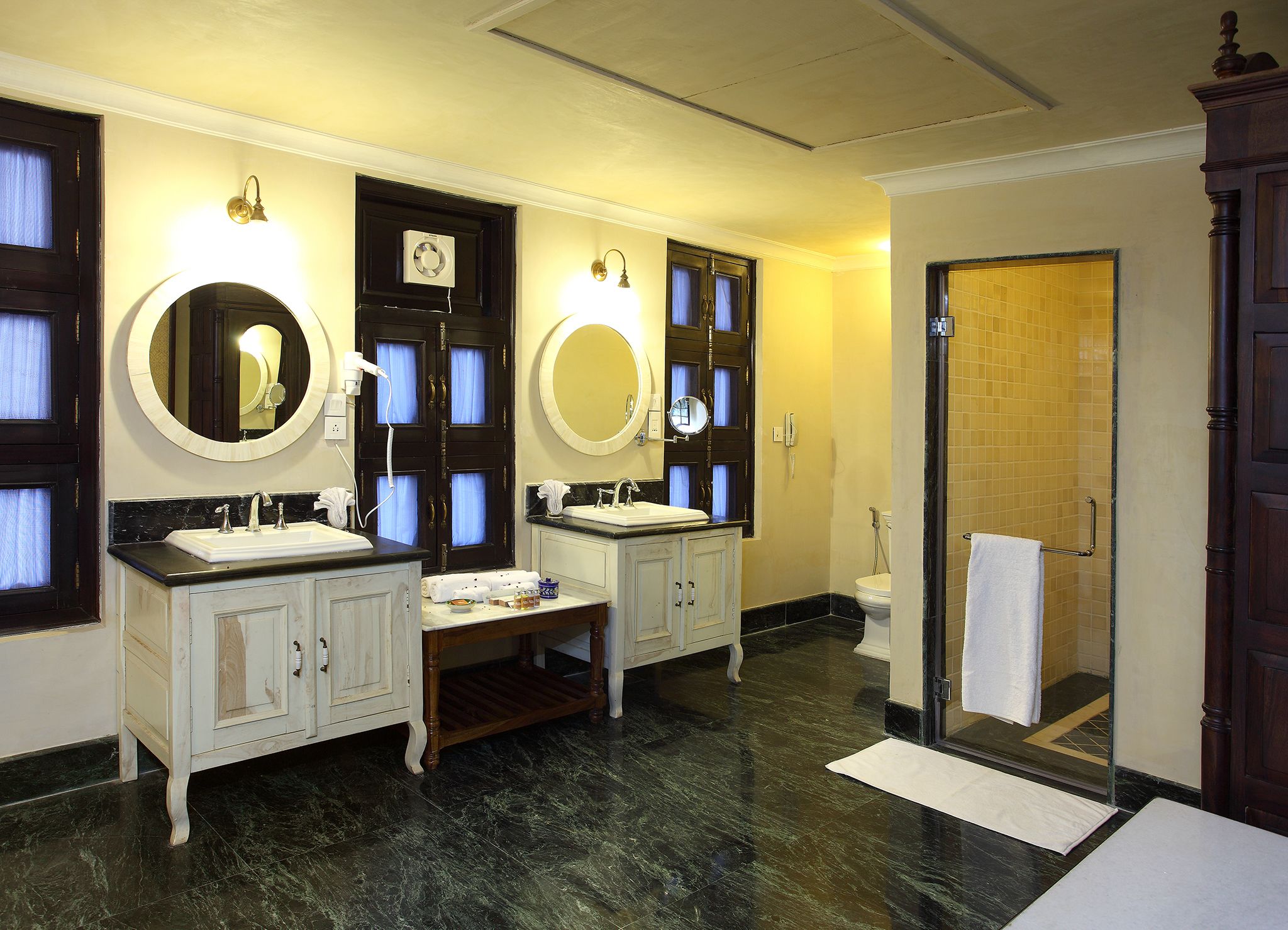Une salle de bain avec deux lavabos, un meuble-lavabo, un miroir, une douche et une porte.