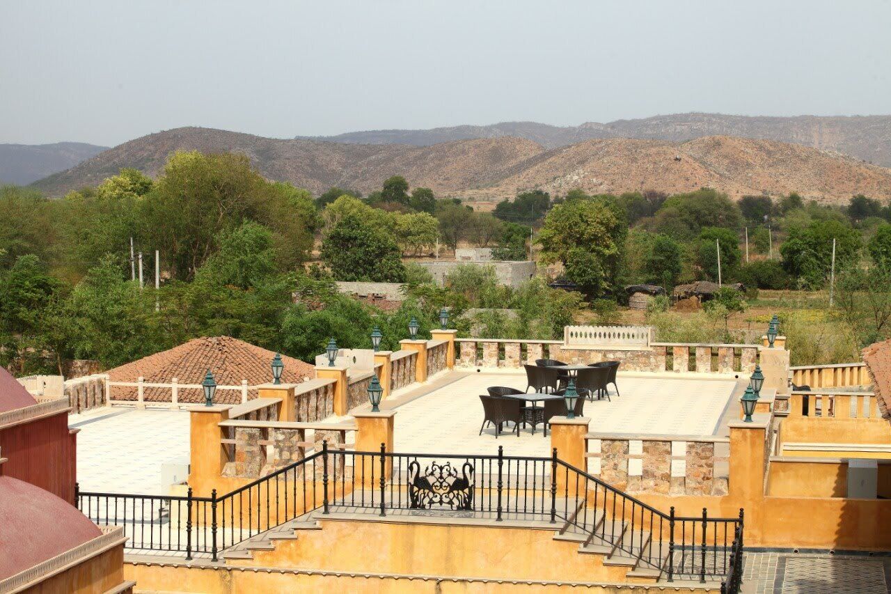A rooftop terrace with outdoor seating, surrounded by greenery and mountains in the background.