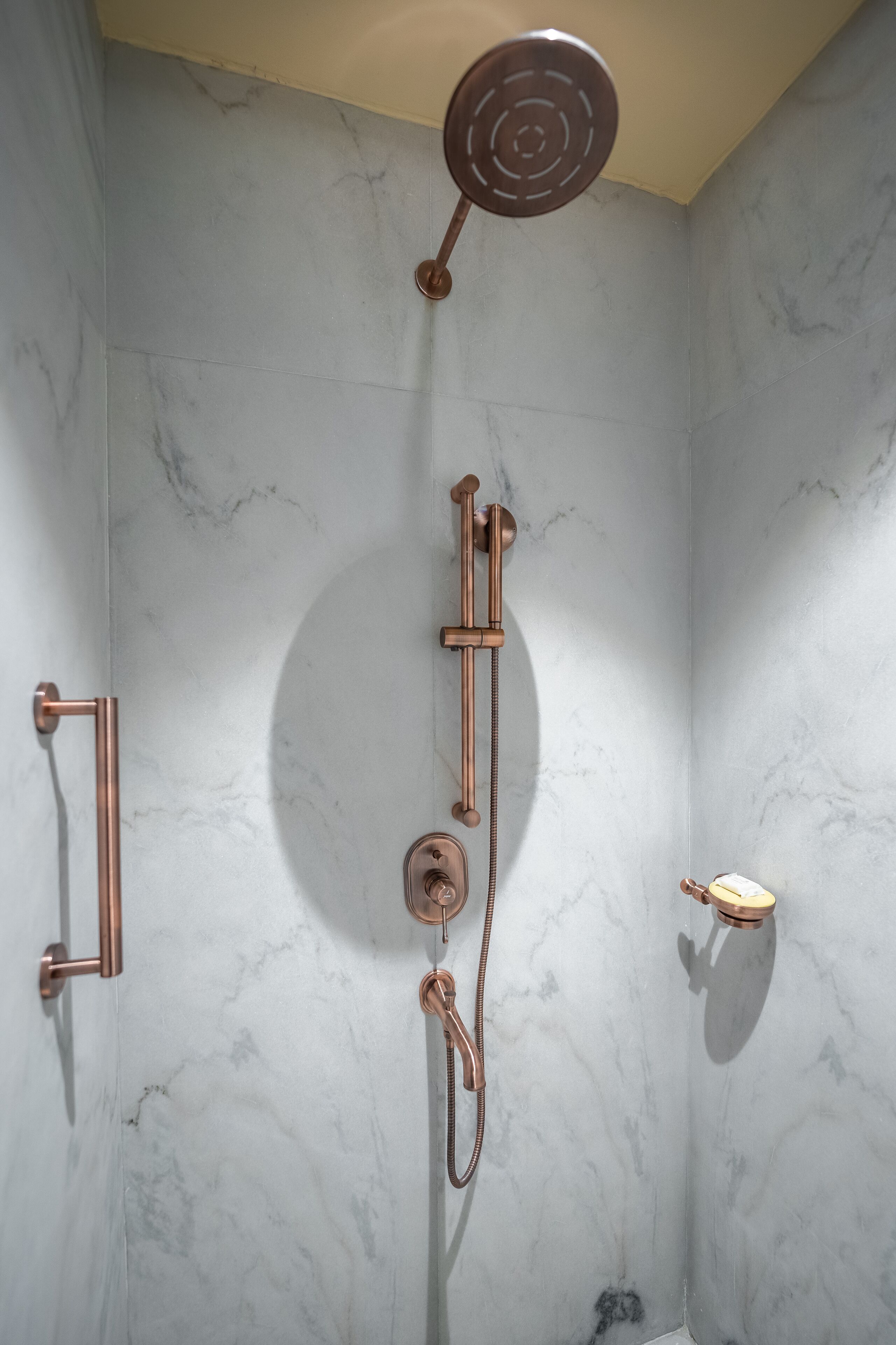 A bathroom with a marble wall, a showerhead, a handheld shower, and a towel rack.