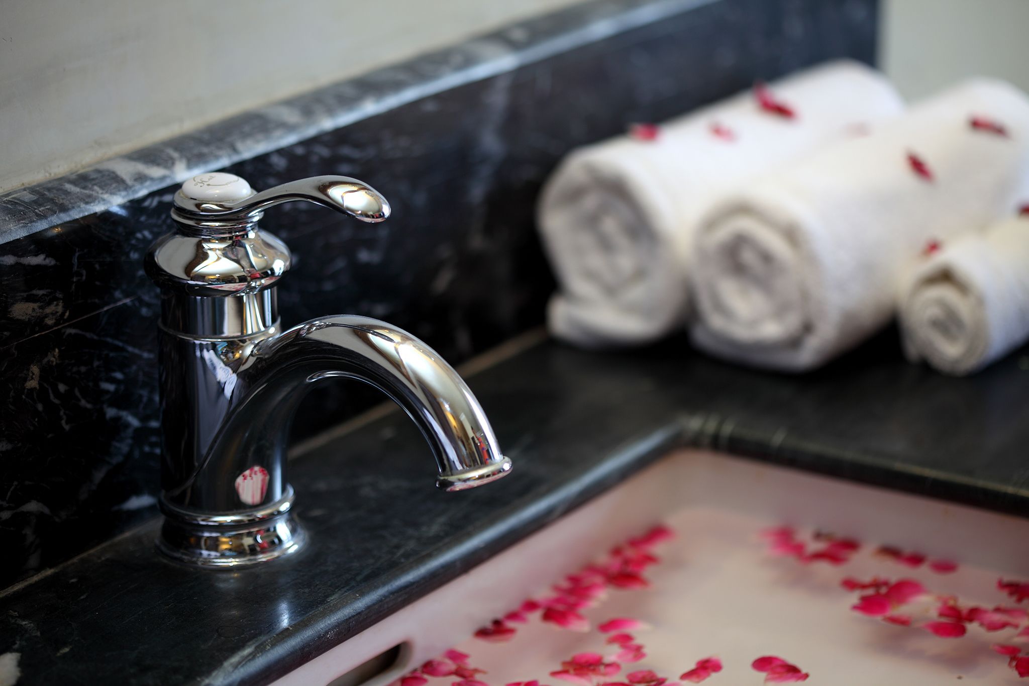 Ein Badezimmer mit chromfarbener Armatur, einer Marmorplatte und gerollten Handtüchern mit Rosenblüten auf dem Waschbecken.