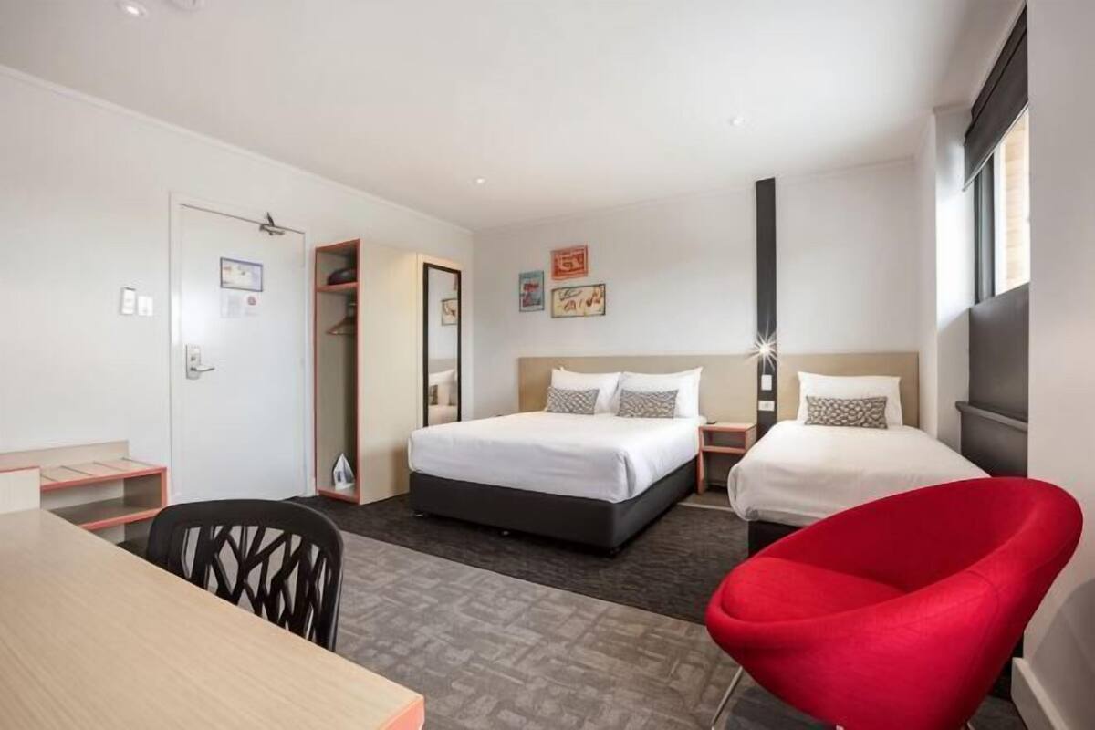 A hotel room with a bed, a desk, a chair, and a wardrobe.