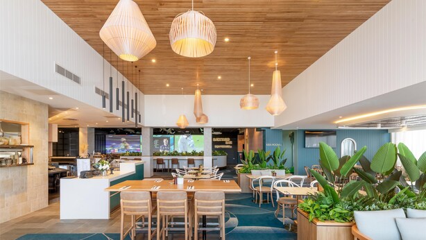 Un restaurante moderno con una isla central, múltiples lámparas colgantes y diversas opciones de asientos, incluyendo mesas y sillas.