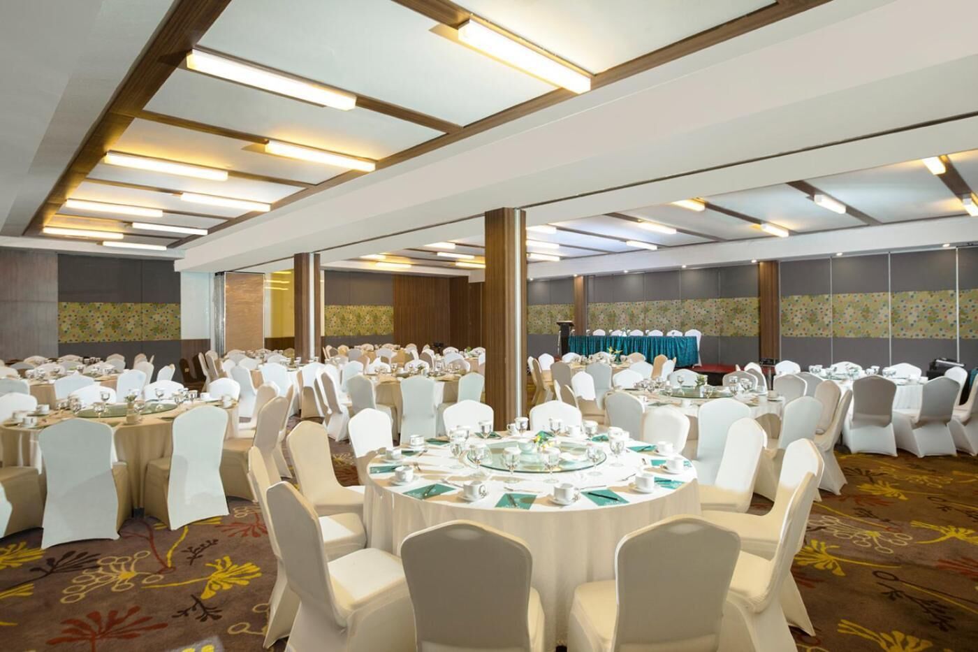 A banquet hall with round tables, white chairs, and a carpeted floor.