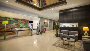 A modern hotel lobby with a reception desk, a seating area with a sofa and armchairs, and a large potted plant. - Khas Pekalongan (Pekalongan)