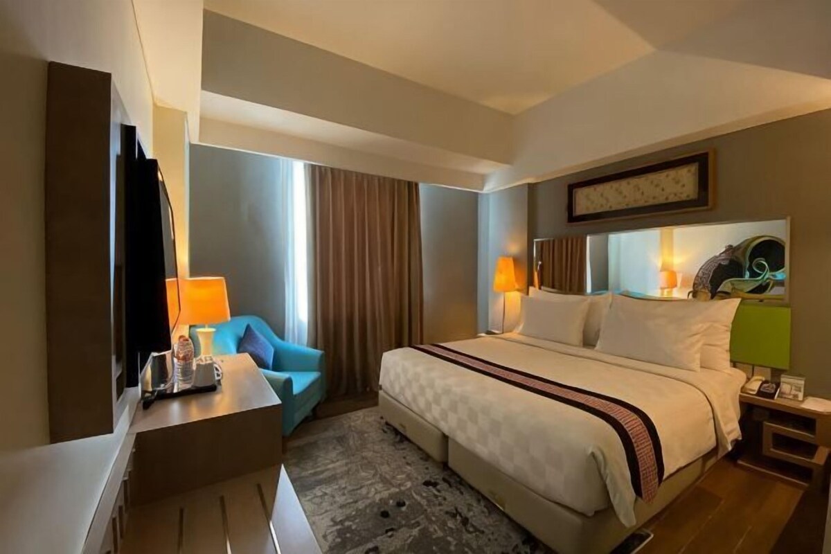 Una habitación de hotel con cama, escritorio, silla, televisor y ventana con cortinas.