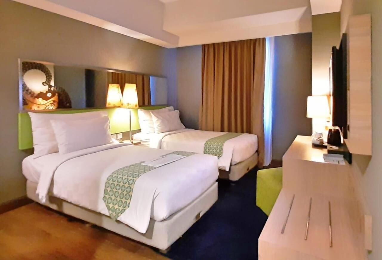 A hotel room with two beds, a desk, a chair, a mirror, and a television.