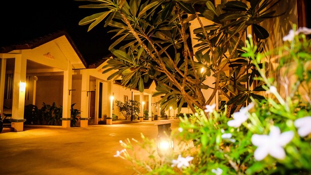 A well-lit hotel entrance with a covered walkway, potted plants, and a clear pathway leading to the building. - Wangthatum (Si Maha Phot)