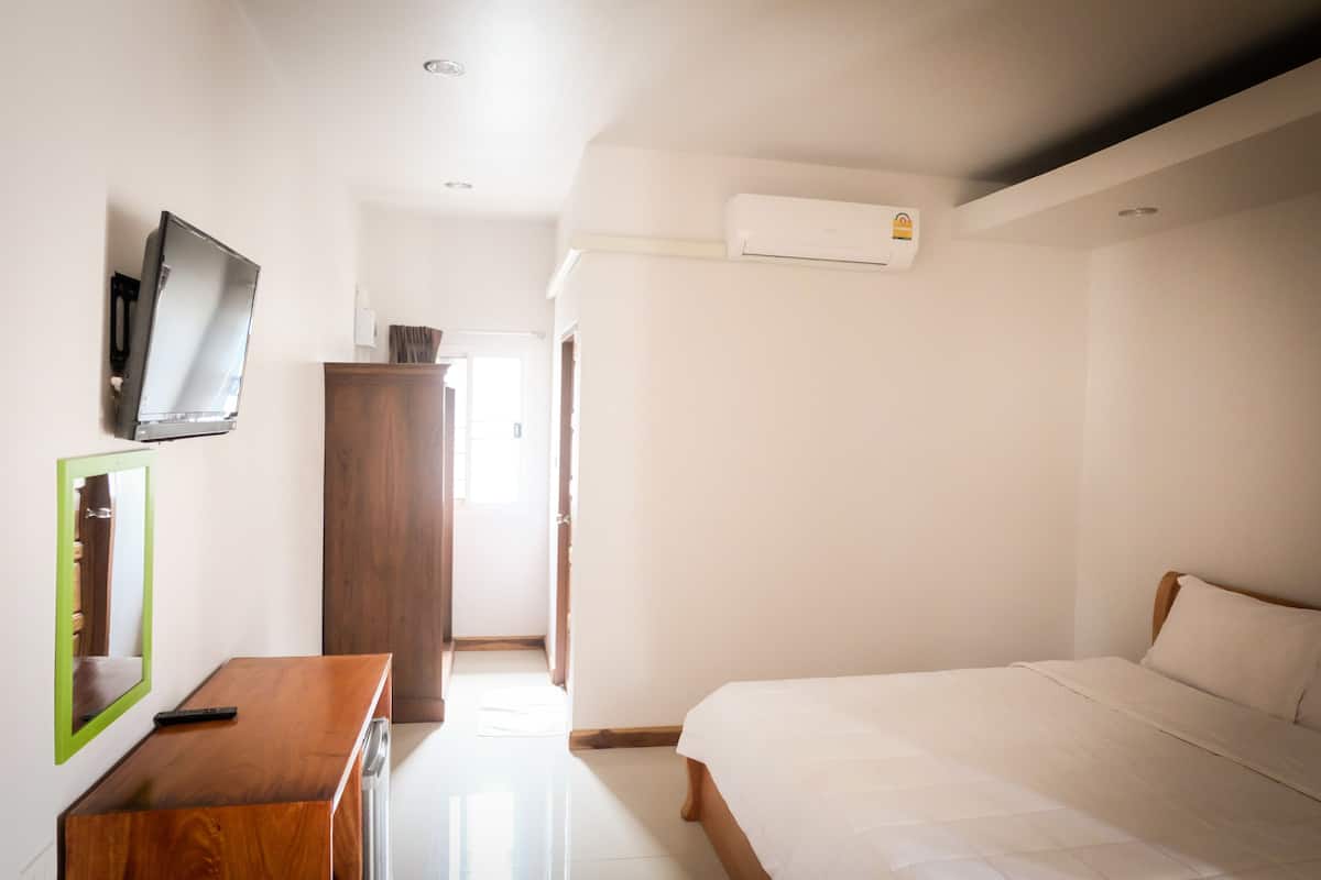 A hotel room with a bed, a wooden desk, a television mounted on the wall, and an air conditioning unit.
