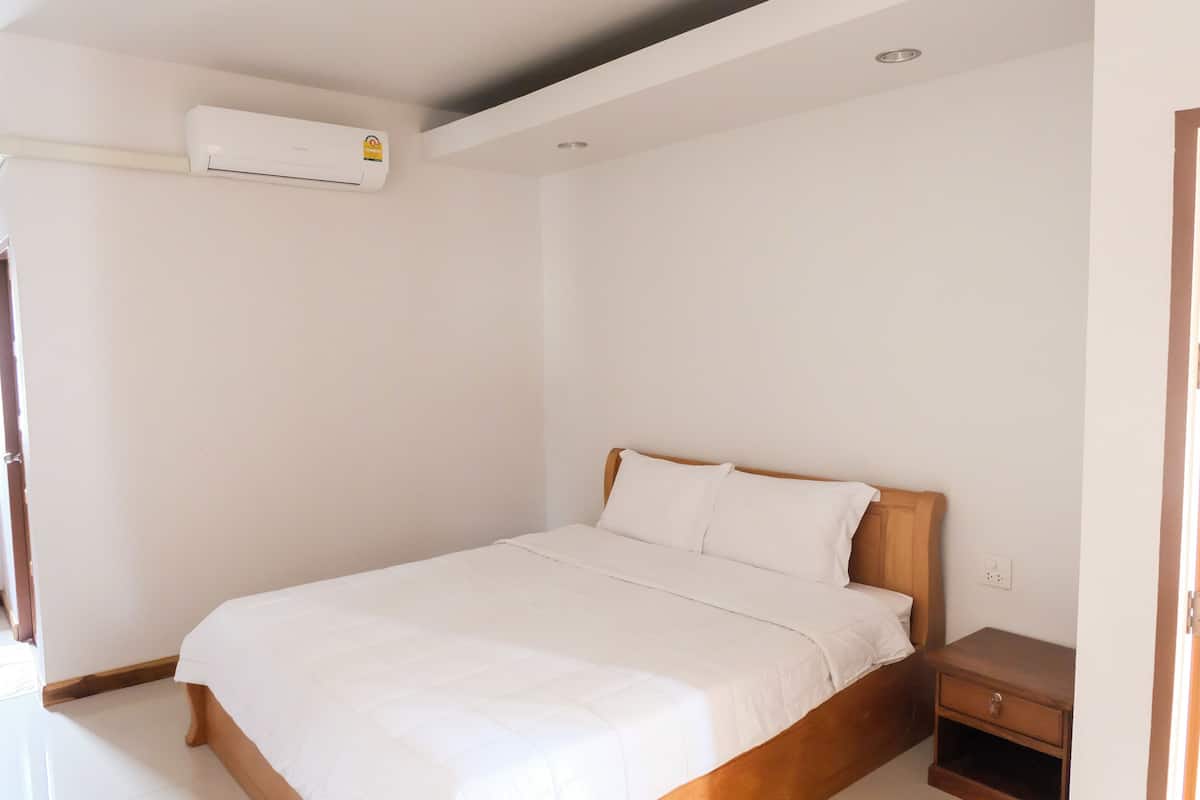 A bedroom with a wooden bed, white bedding, a nightstand, and a wall-mounted air conditioner.