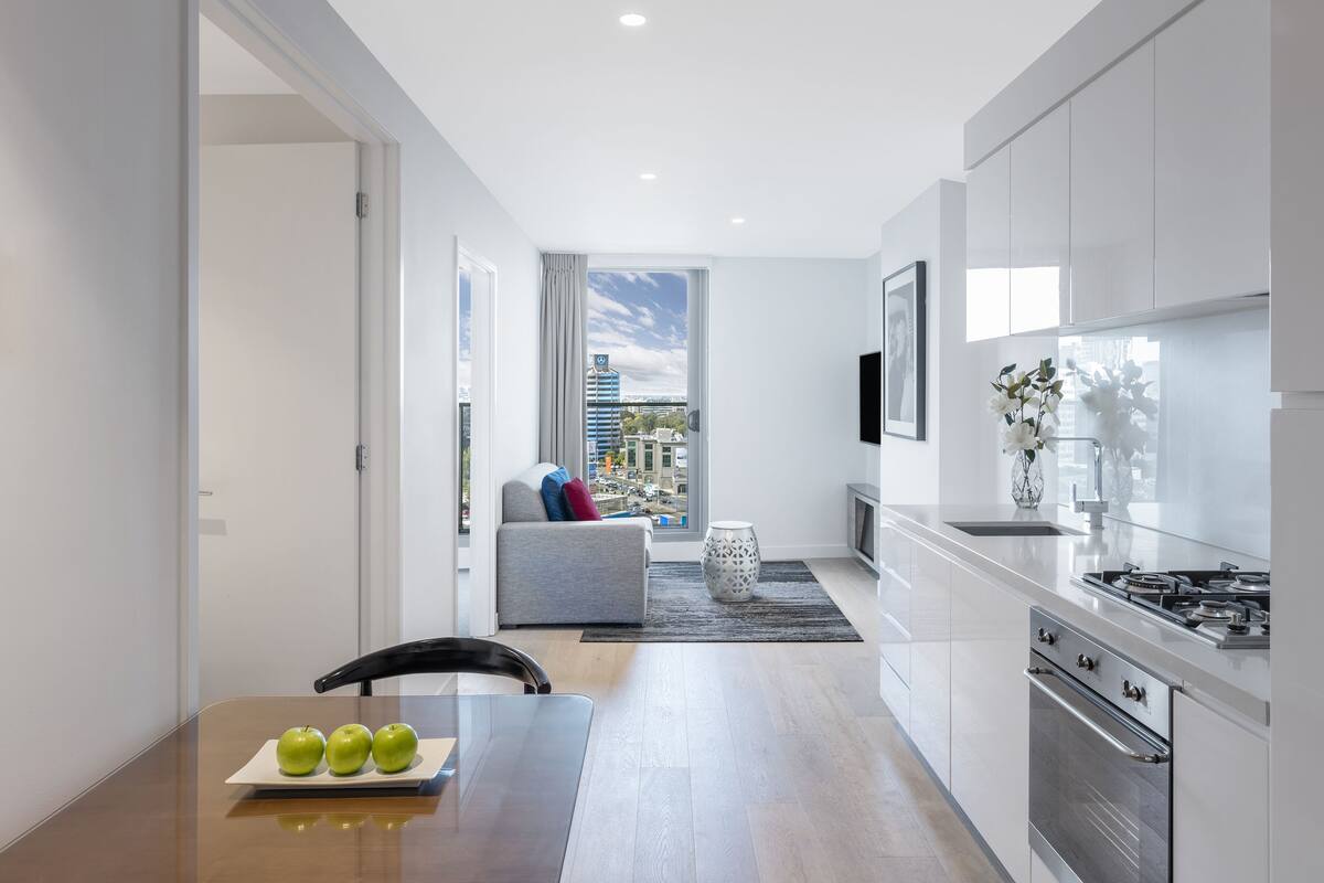 Una cocina moderna con vistas a la ciudad, un comedor con mesa y sillas, y un espacio de sala de estar con sofá y elementos decorativos.