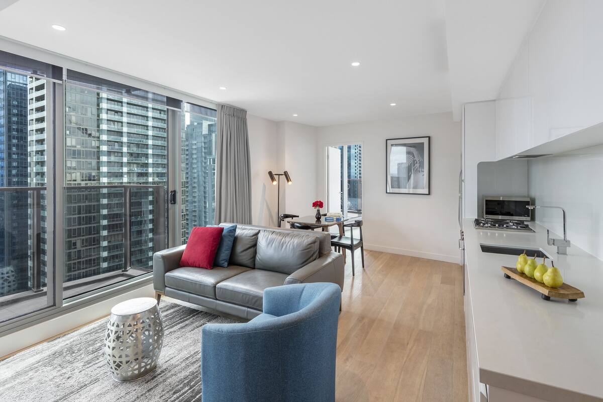 Una sala moderna con un sofá gris, un sillón azul y un comedor con mesa y sillas.