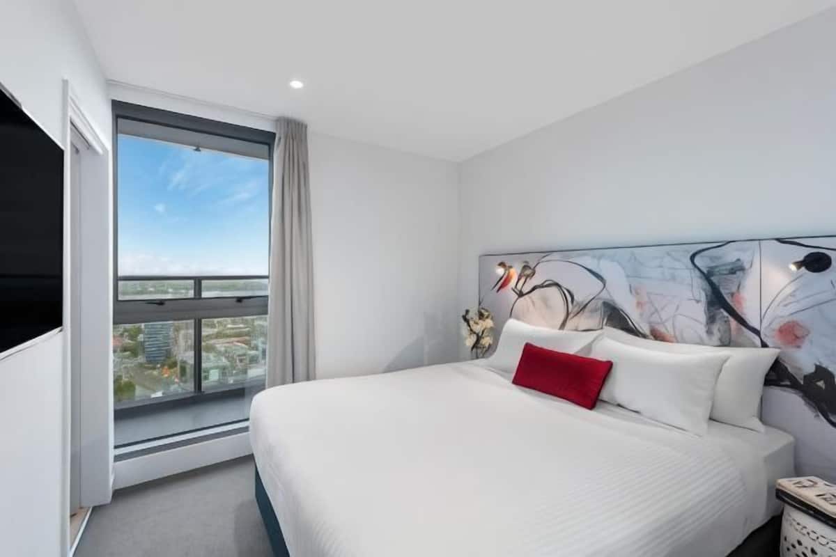 Una habitación de hotel moderna con una cama grande, vistas a la ciudad y una original obra de arte abstracta en la pared.