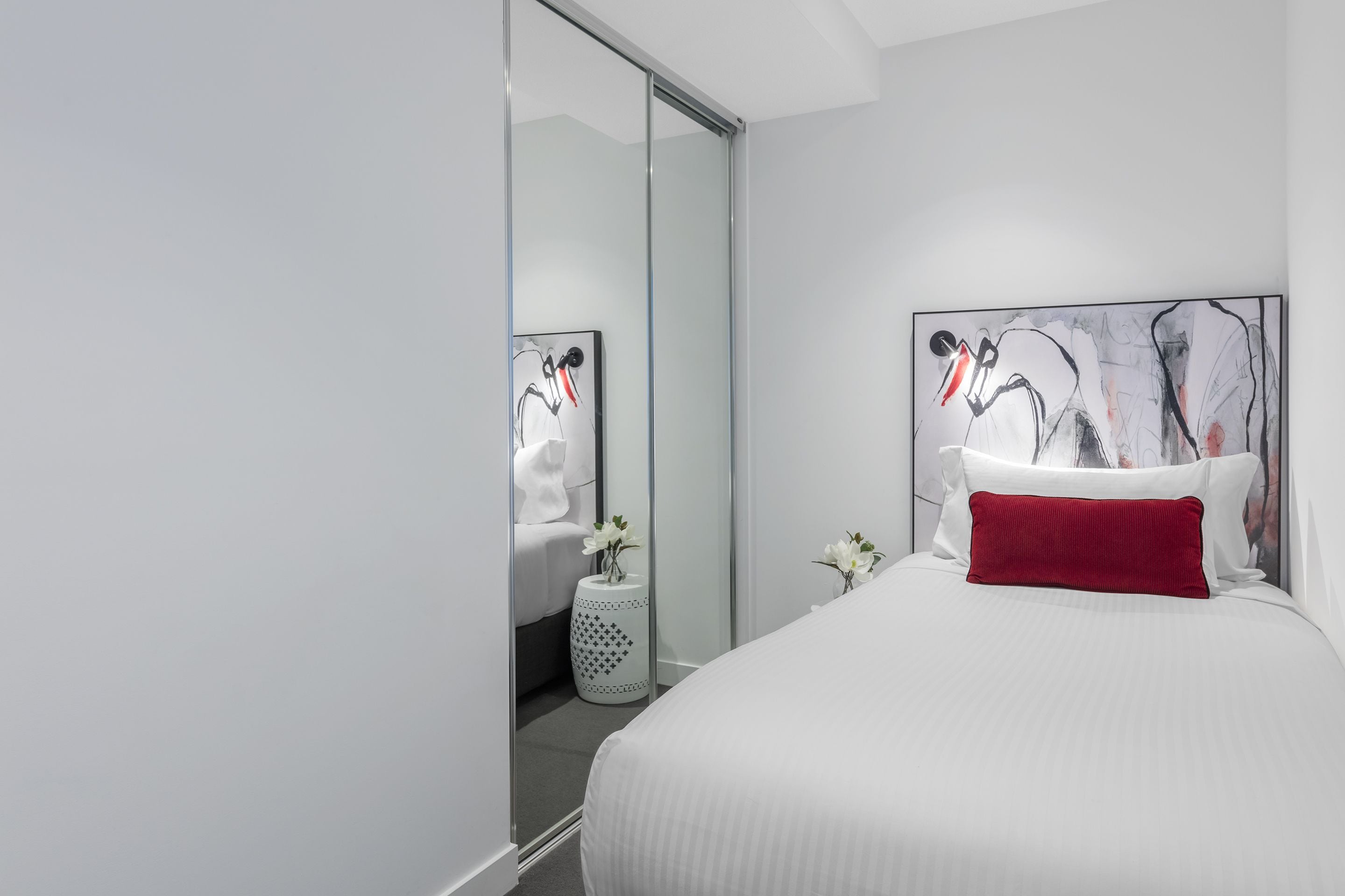 Een moderne hotelkamer met een groot bed, een glazen scheidingswand en abstracte kunstwerken aan de muren.