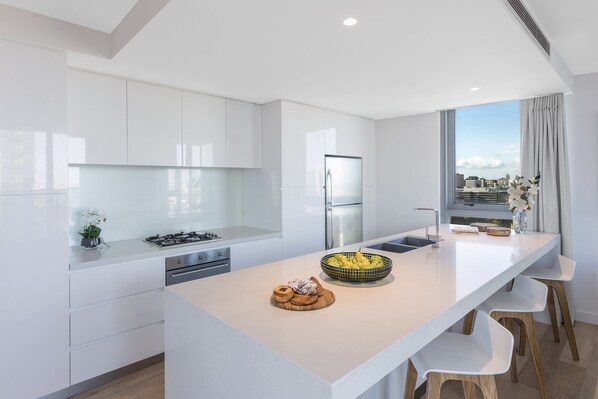 Una cocina moderna con armarios blancos, una isla central y vistas a la ciudad a través de grandes ventanales.