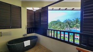 A bathroom with a freestanding bathtub, a window with a view of a pool and palm trees, and a wooden bench. - Sand & Sandals Desaru Beach Resort & Spa (Bandar Penawar)