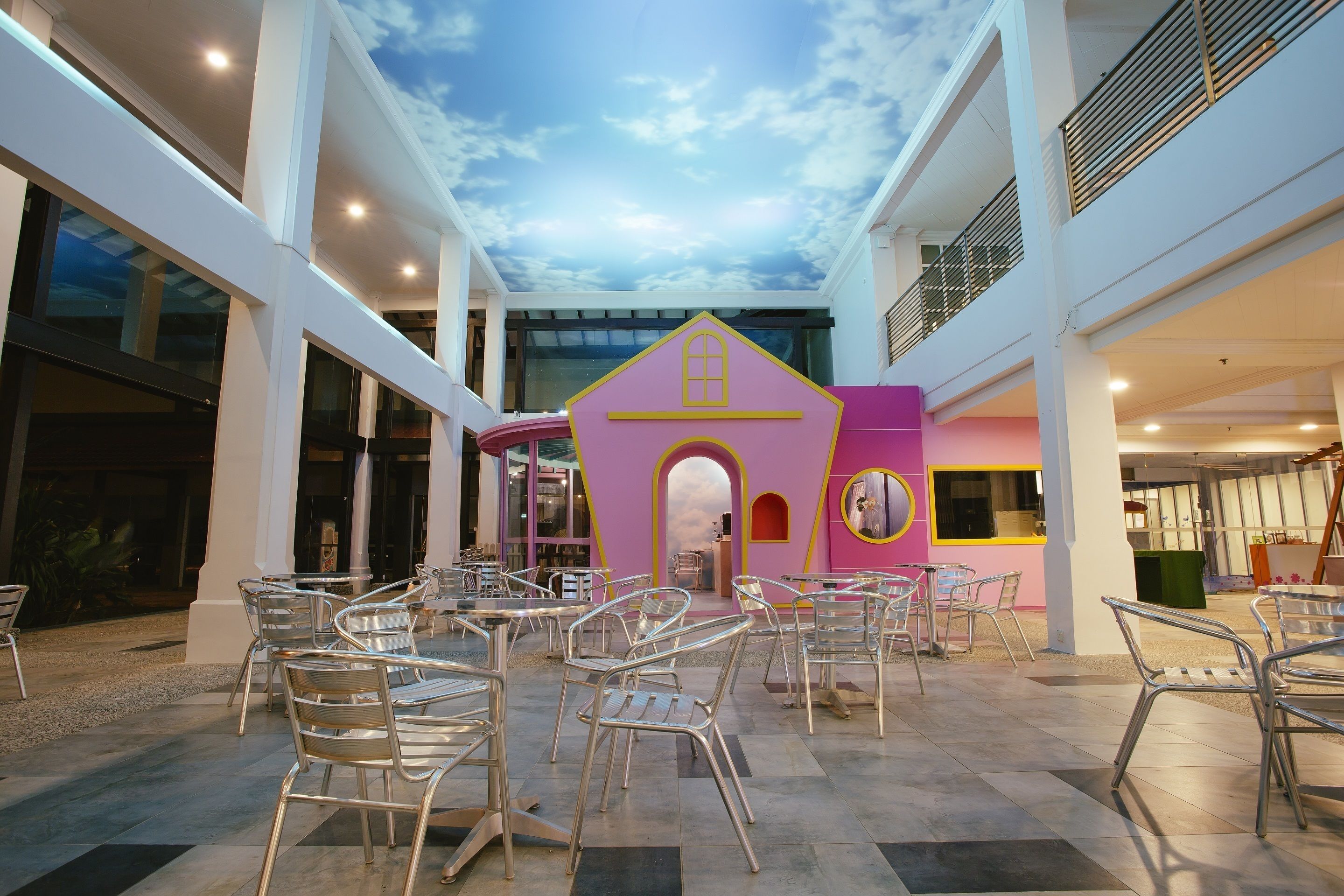 A spacious indoor area with multiple tables and chairs, a pink playhouse, and a large window offering a view of the sky.
