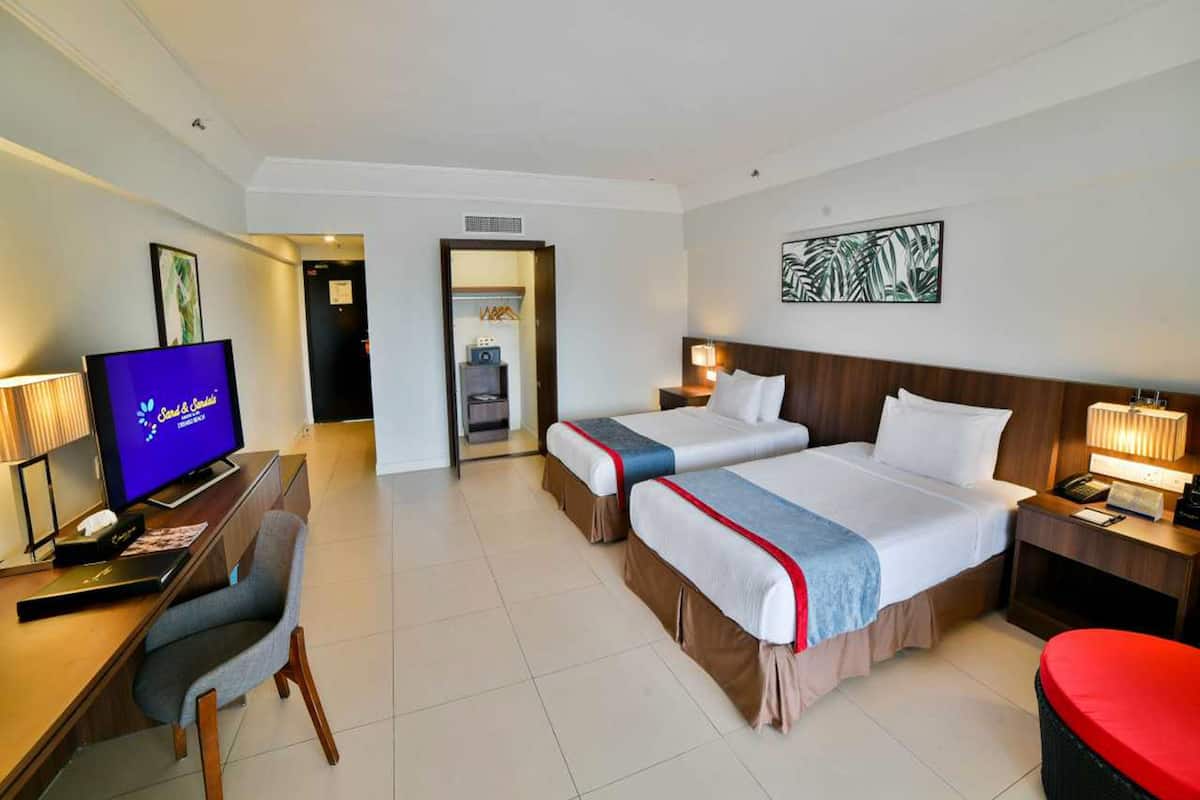 A hotel room with two beds, a desk with a computer, a TV, and a red ottoman.
