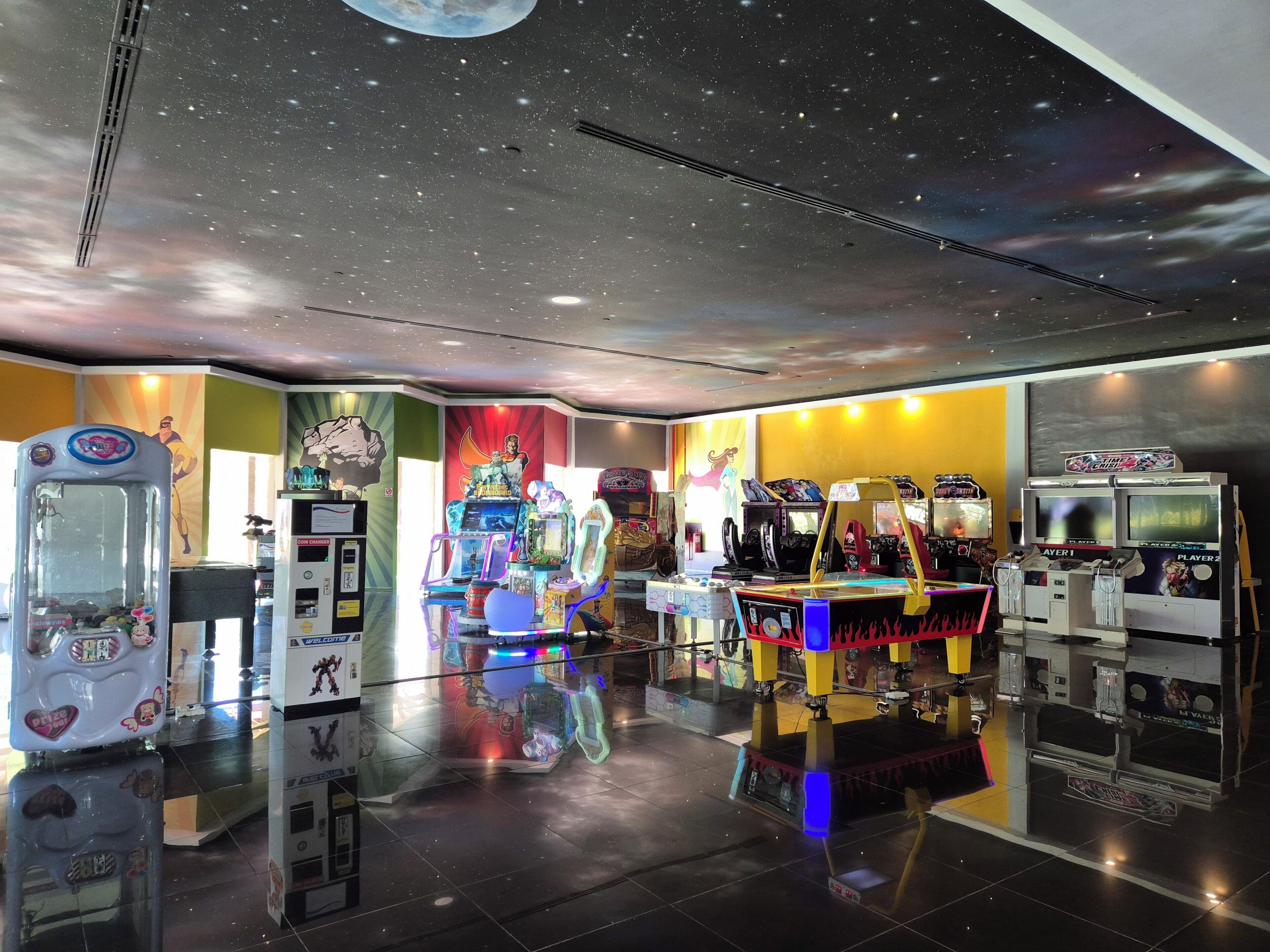 Une salle d’arcade avec différents jeux et un plafond étoilé.