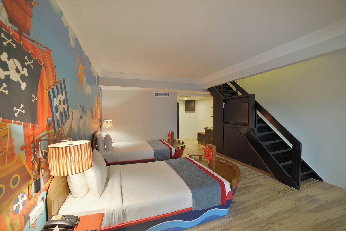 A hotel room with a bed, a desk, a chair, a lamp, and a TV.