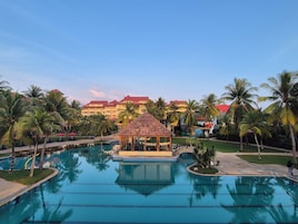Un resort con una gran piscina, palmeras y un edificio de techo rojo al fondo.