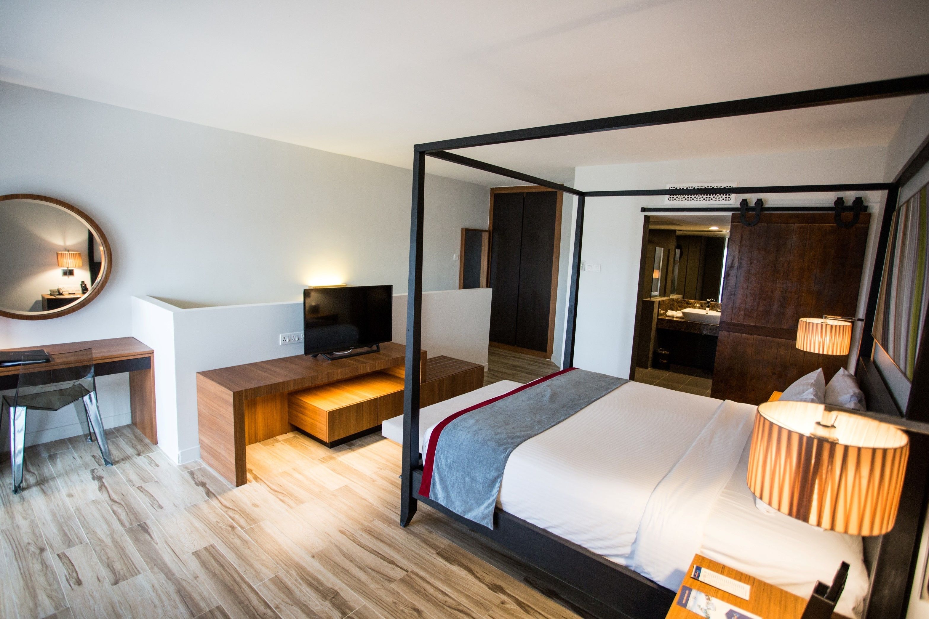Une chambre d’hôtel moderne avec un lit à baldaquin, un bureau avec un ordinateur, une télévision et un miroir.