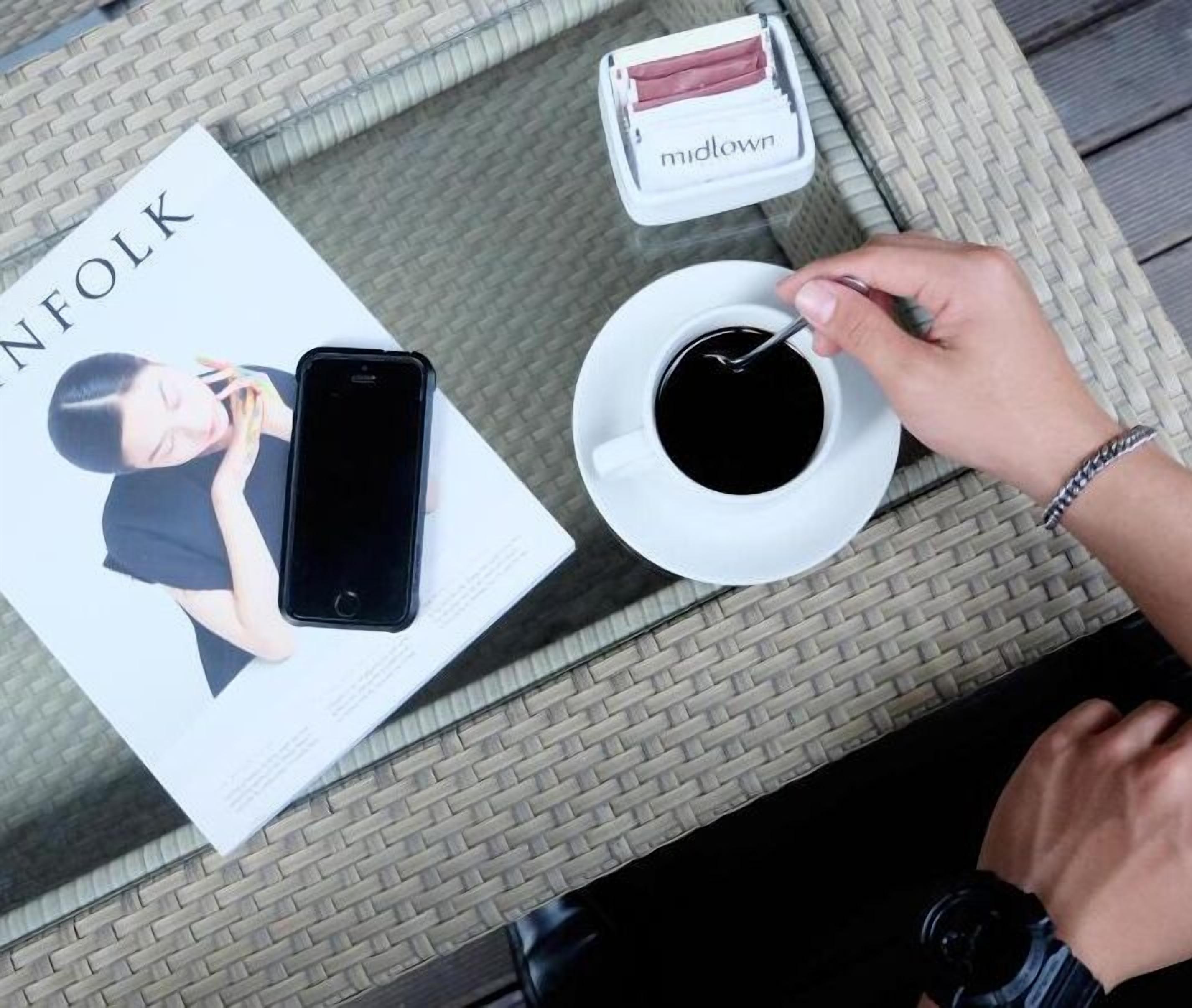 A table with a magazine, a smartphone, a cup of coffee, and a small box of tissues.