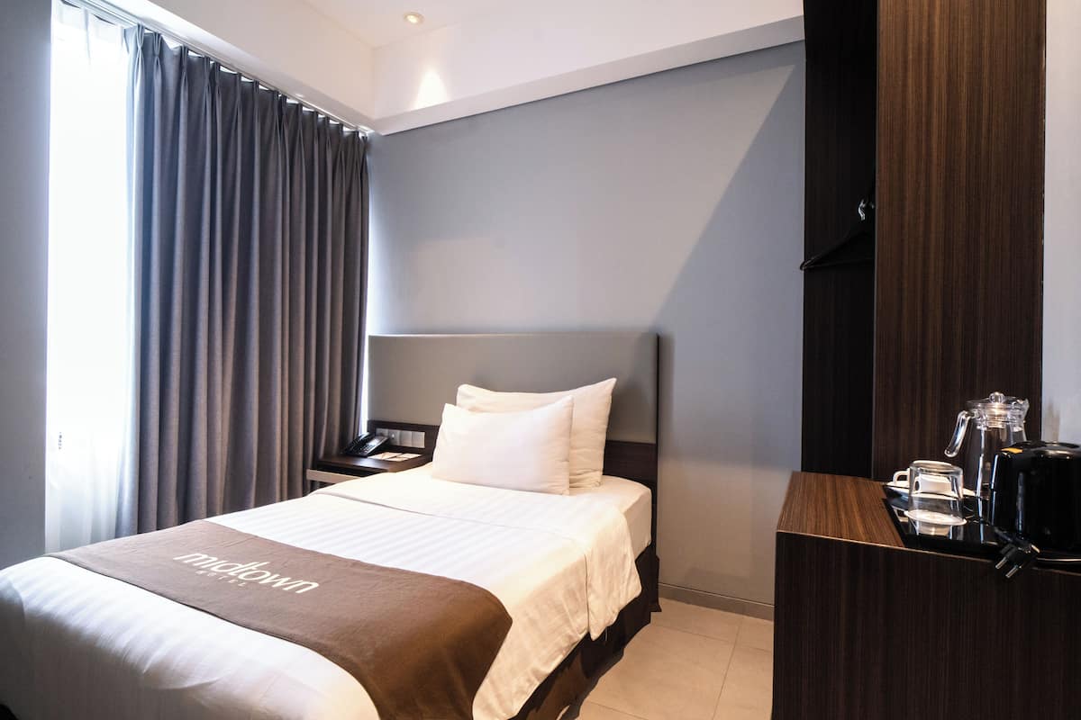 A hotel room with a bed, a nightstand, a coffee maker, and a desk with a chair.