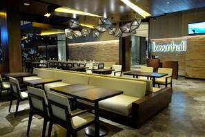 Un restaurante moderno con cabinas y mesas, un muro decorativo de madera y una pantalla de televisión que muestra a una persona.