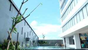 Ein Pool im Freien mit modernem Design, umgeben von Grünpflanzen und einem Gebäude mit großen Fenstern.