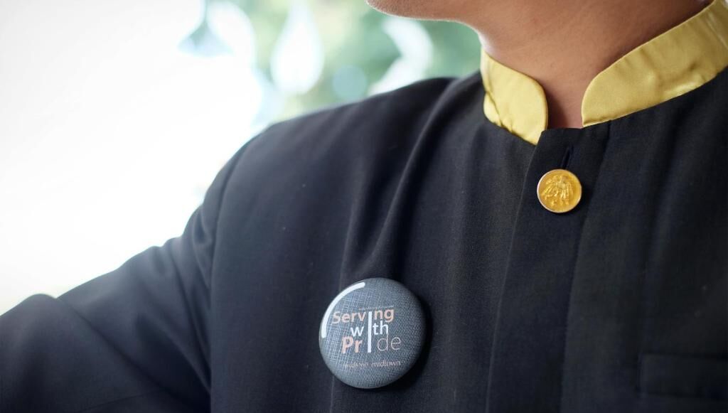 A person wearing a black shirt with a gold button and a badge that reads "Serving with Pride."