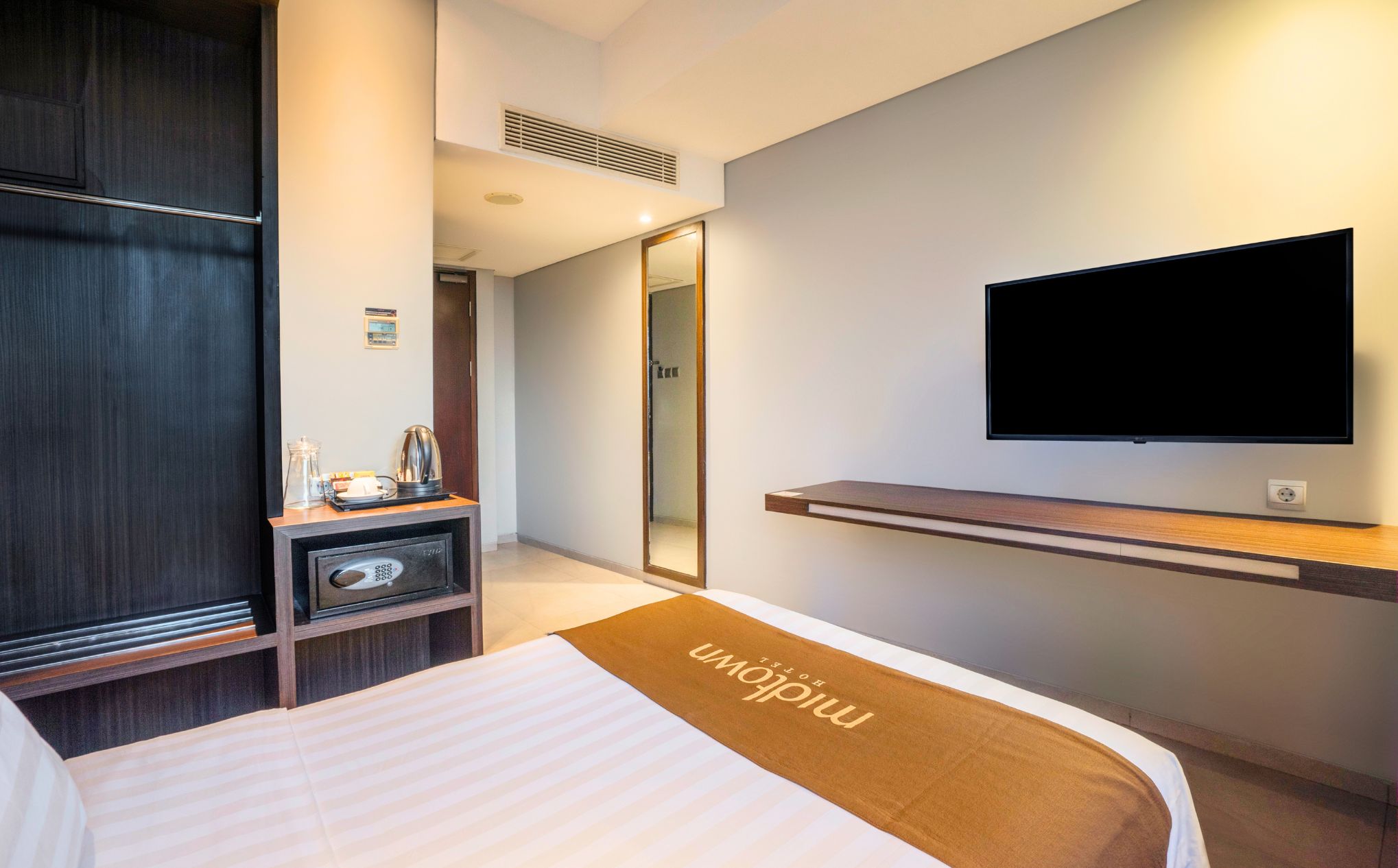 A hotel room with a bed, a television mounted on the wall, a minibar, and a mirror.