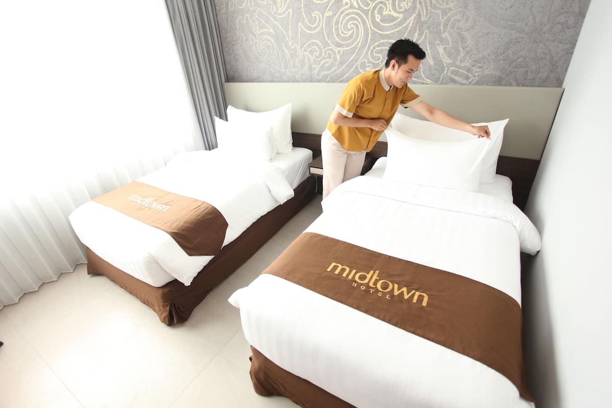 A hotel room with two beds, each with a brown headboard and a white bedspread. The room has a modern design with a patterned wall and a large window with curtains.