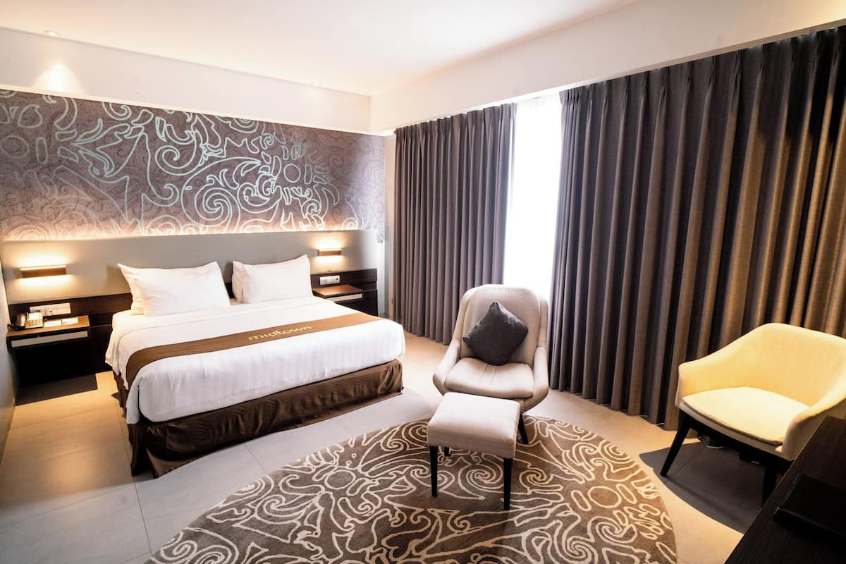 A hotel room with a large bed, two bedside tables, a chair, a rug, and a curtain.
