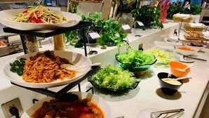 Un bufé con diversos platos, entre ellos fideos, ensaladas y un bol de sopa.