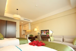 Habitación de hotel con cama, sofá, escritorio con computadora, televisor y zona de comedor.