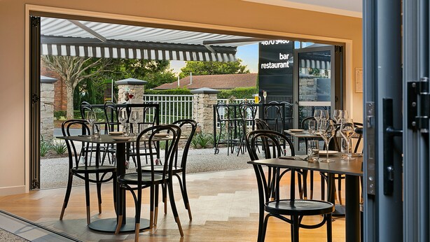 Een eetruimte met tafels en stoelen, met uitzicht op terras, en een bordje met de tekst 'bar restaurant'.