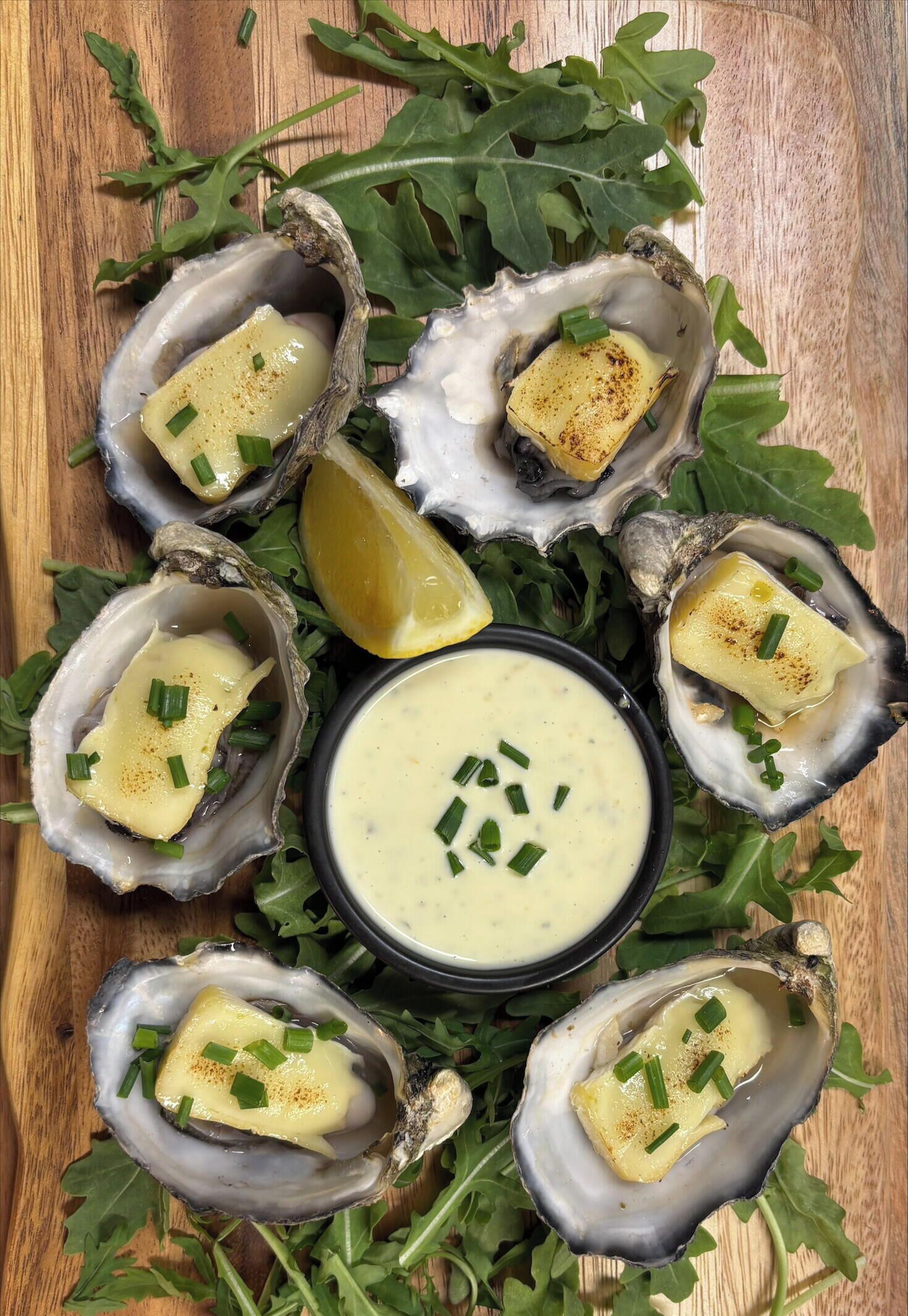 Et træbord med østers, citron og en cremet sauce.