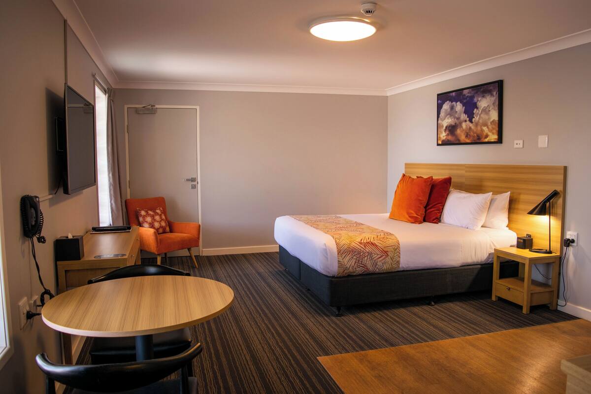 Une chambre d’hôtel avec un lit, un bureau, une chaise, une table et un tableau au mur.