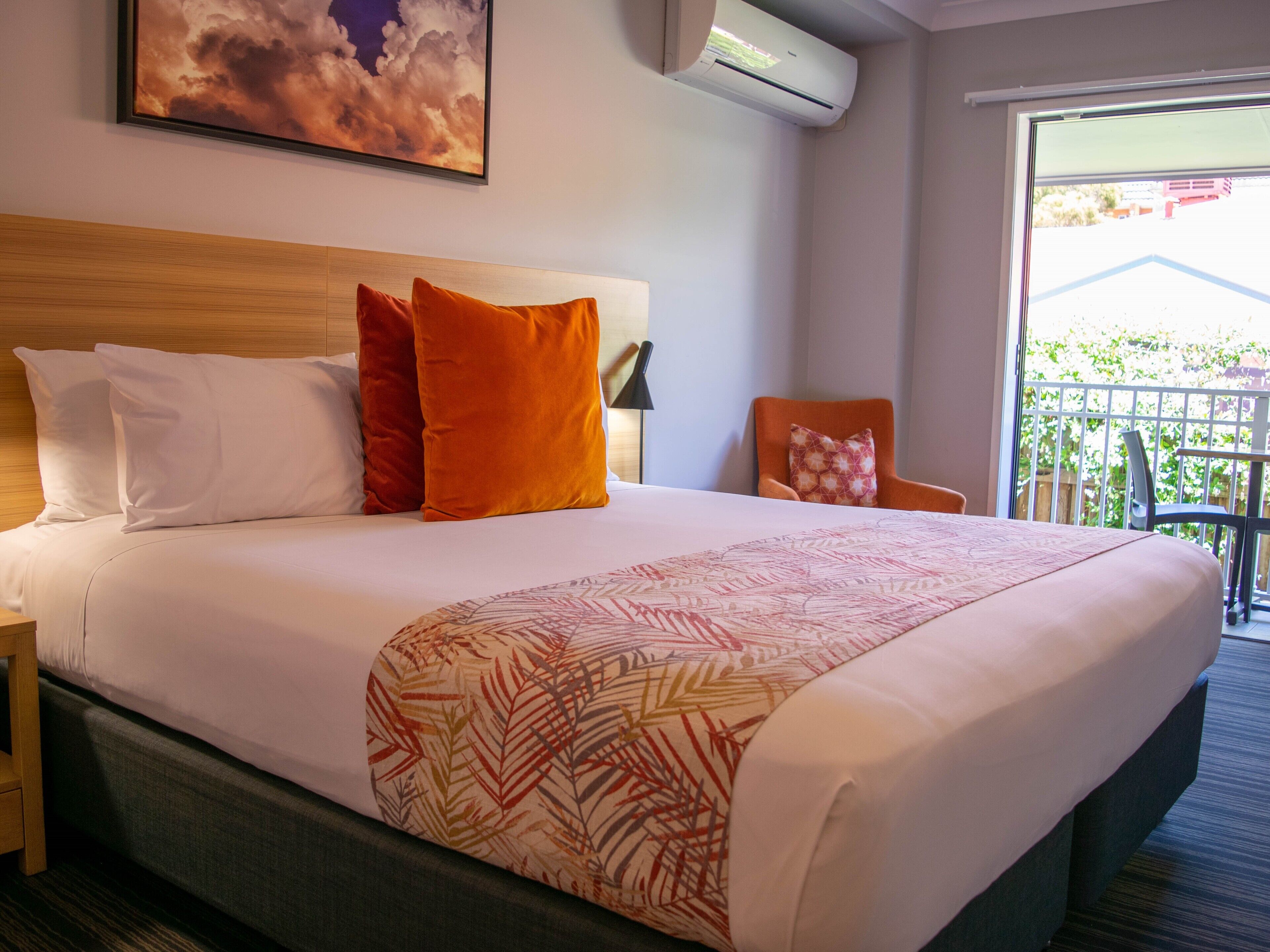 Une chambre d’hôtel avec un grand lit, une tête de lit en bois, un balcon avec vue et un appareil de climatisation.