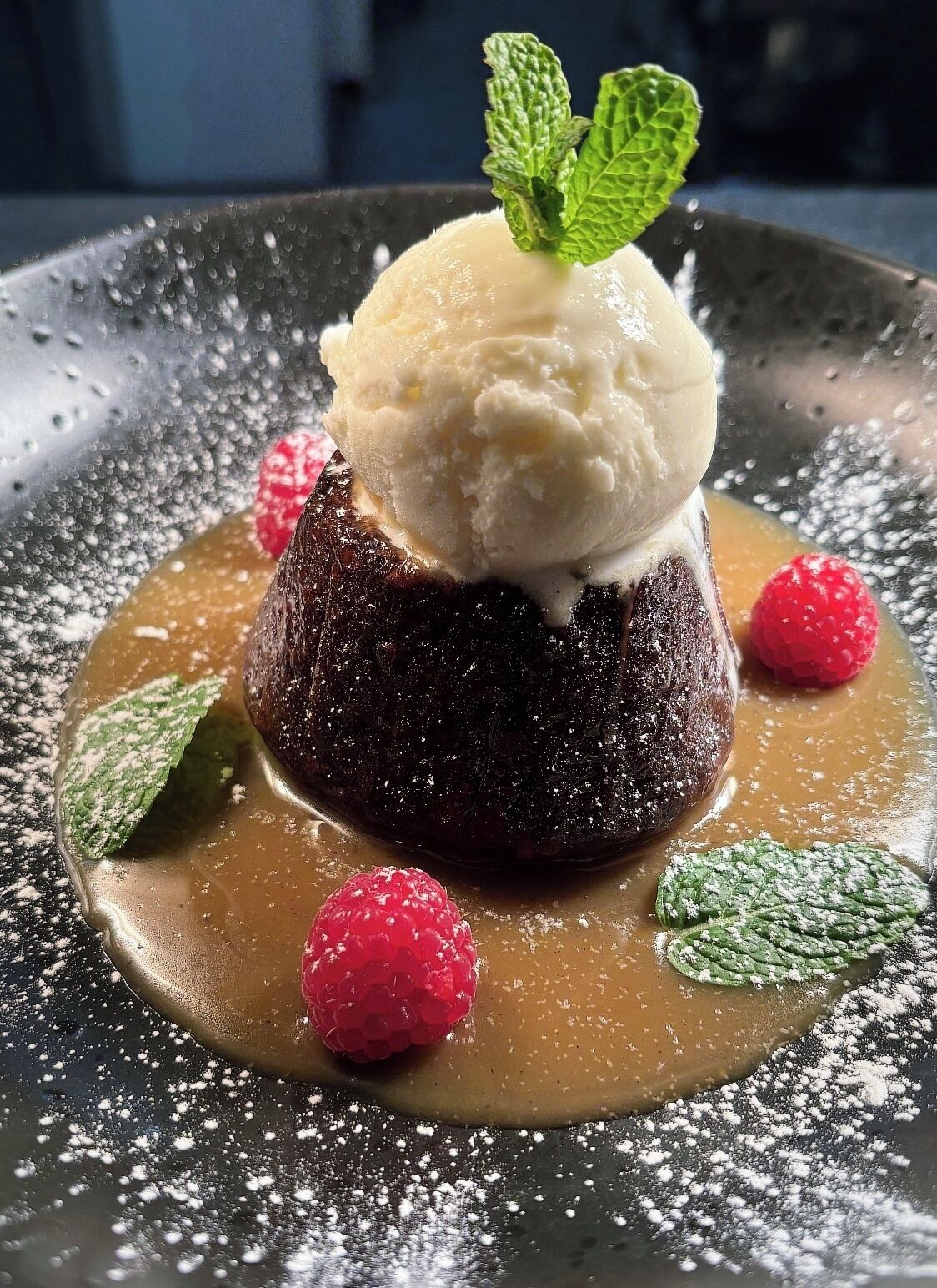 A dessert with a scoop of ice cream on top, surrounded by raspberries and mint leaves.