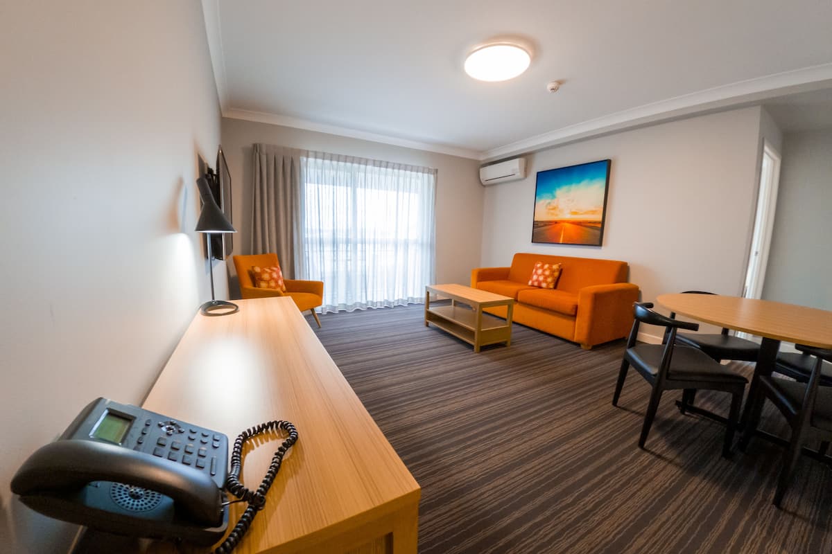 Une chambre d’hôtel avec un bureau en bois, un téléphone, un canapé orange, une table basse et un tableau au mur.