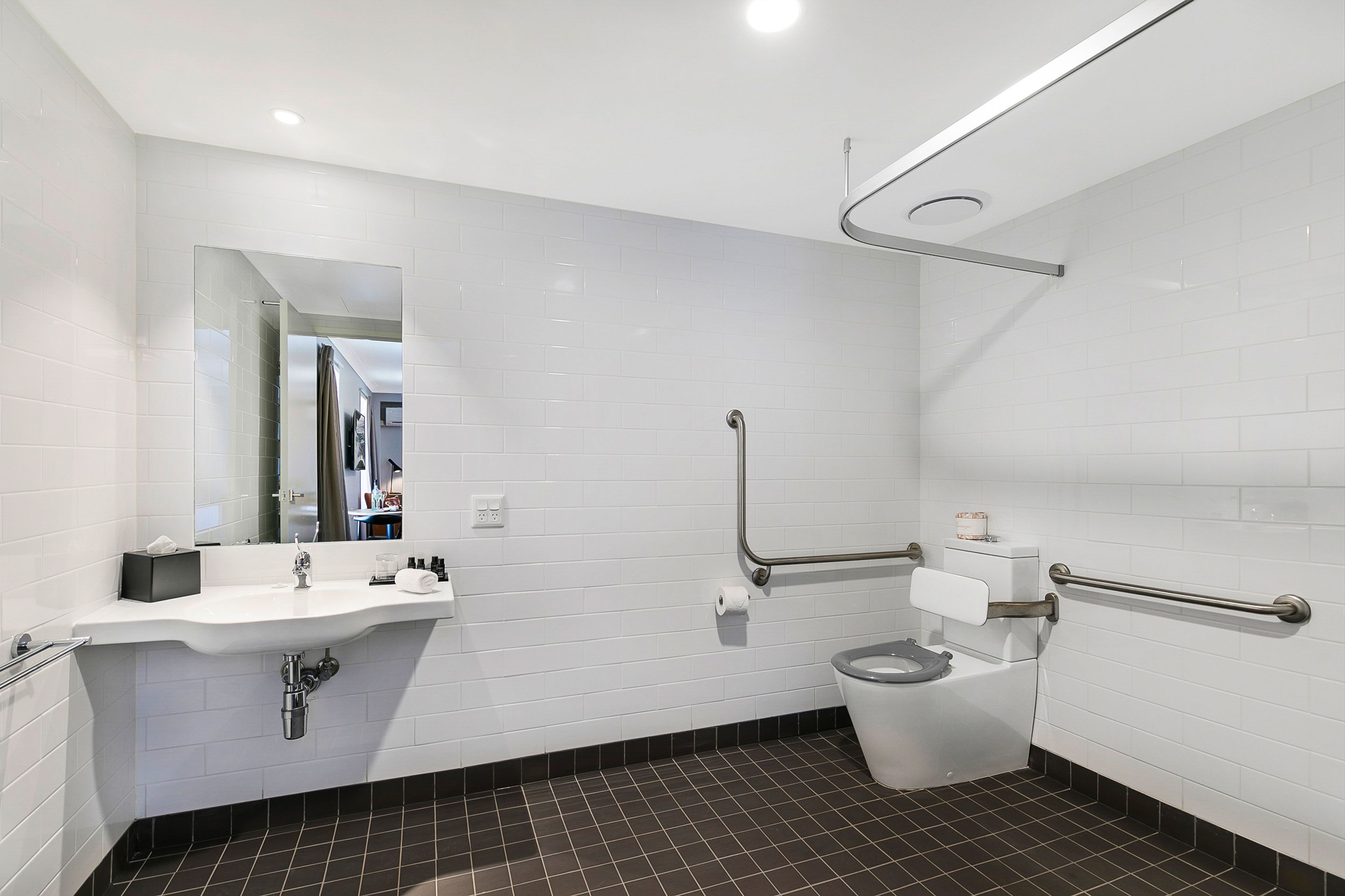 A modern bathroom with white tiles, a sink, a toilet, and a mirror.