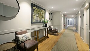Een hotelgang met een receptiebalie, een zithoek en deuren naar de kamers.