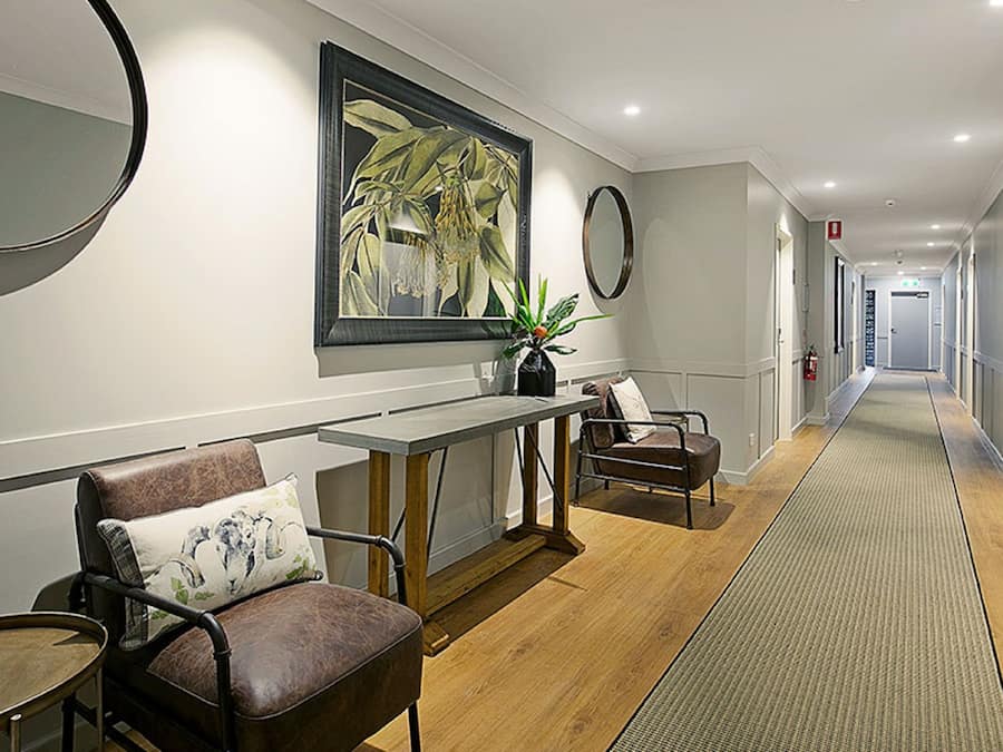 Un couloir d’hôtel avec un comptoir d’accueil, un espace salon et des portes donnant accès aux chambres.