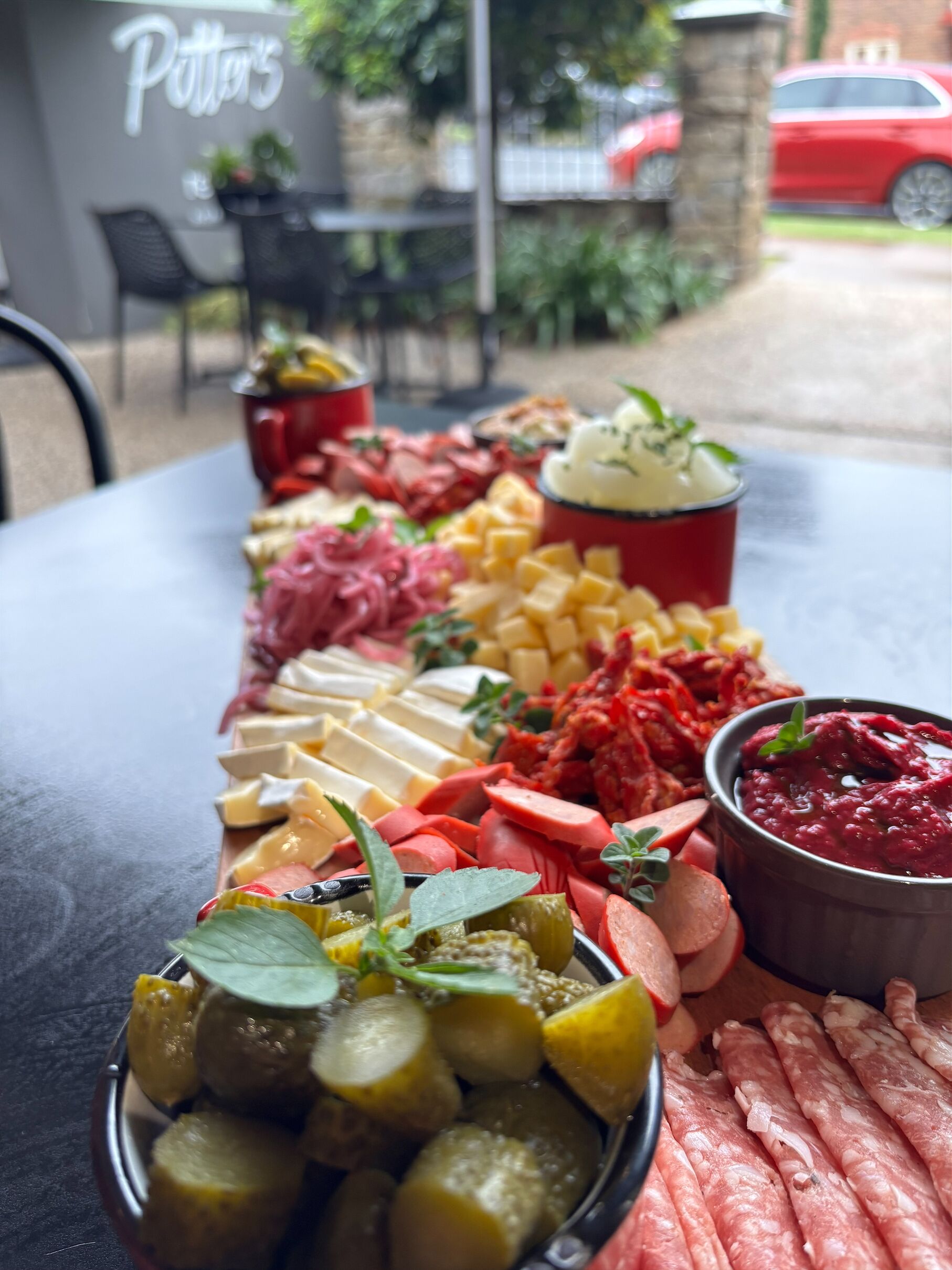 A charcuterie board with various meats, cheeses, and pickles on a table outside a restaurant.